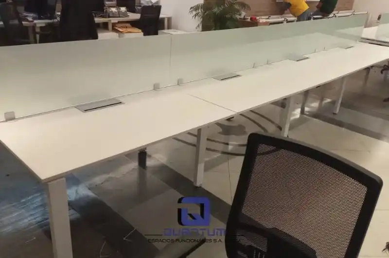 Diseño moderno de estaciones de trabajo colaborativas con mamparas, fomentando la interacción en una oficina en la Ciudad de México.