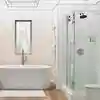 Canceles para baño de vidrio en cdmx Moderno cancel de ducha y tina con puertas de cristal corredizas y herrajes en color oscuro, en un baño con azulejos claros