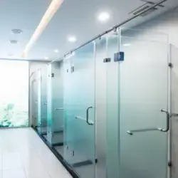 Instalación de mamparas de vidrio templado con acabado esmerilado degradado y canceles para duchas en 48 suites de hotel boutique en Zacatecas Centro con herrajes cromados minimalistas