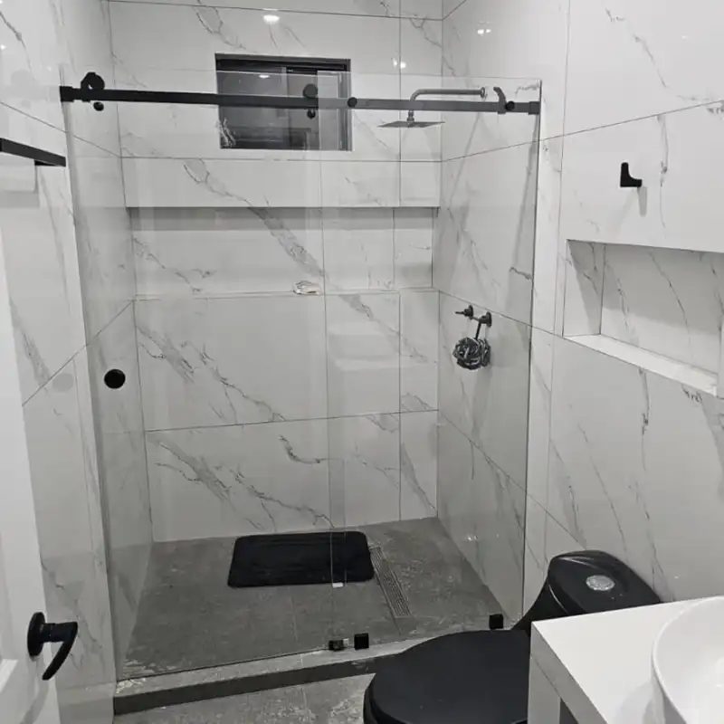 Cancel de vidrio templado de 8 mm con herrajes en acero negro mate instalado en suite de lujo con revestimiento mármol en Tangolunda, Huatulco, Oaxaca