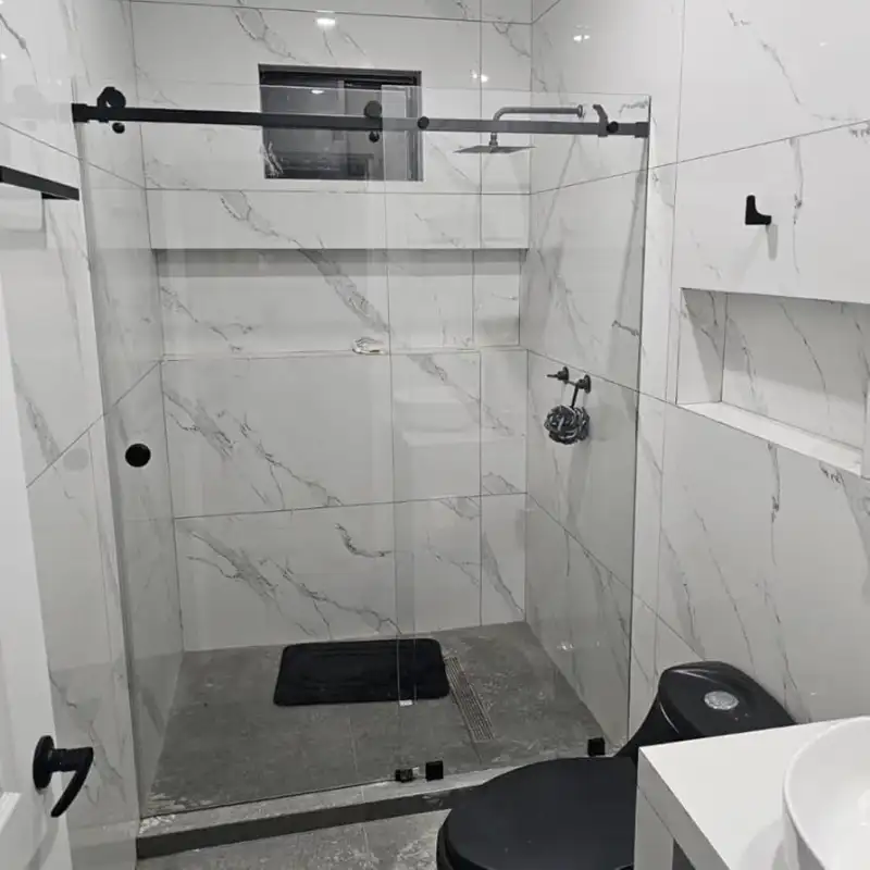 Cancel de vidrio templado corredizo instalado en baño premium con acabados en mármol blanco y herraje negro mate en Del Valle, Alcaldía Benito Juárez, Ciudad de México