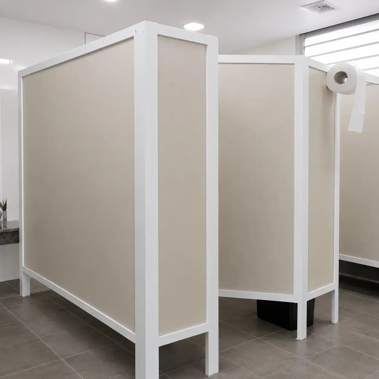 Mamparas de acrílico color arena enmarcadas en perfil blanco, montadas sobre piso de porcelanato gris con dispensador de papel — Mamparas Sanitarias Mineral de la Reforma.